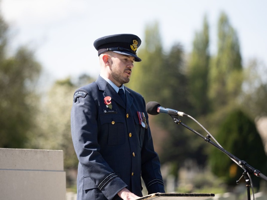 A man in uniform gives a speech from a lectern in front of the war memorial wall.