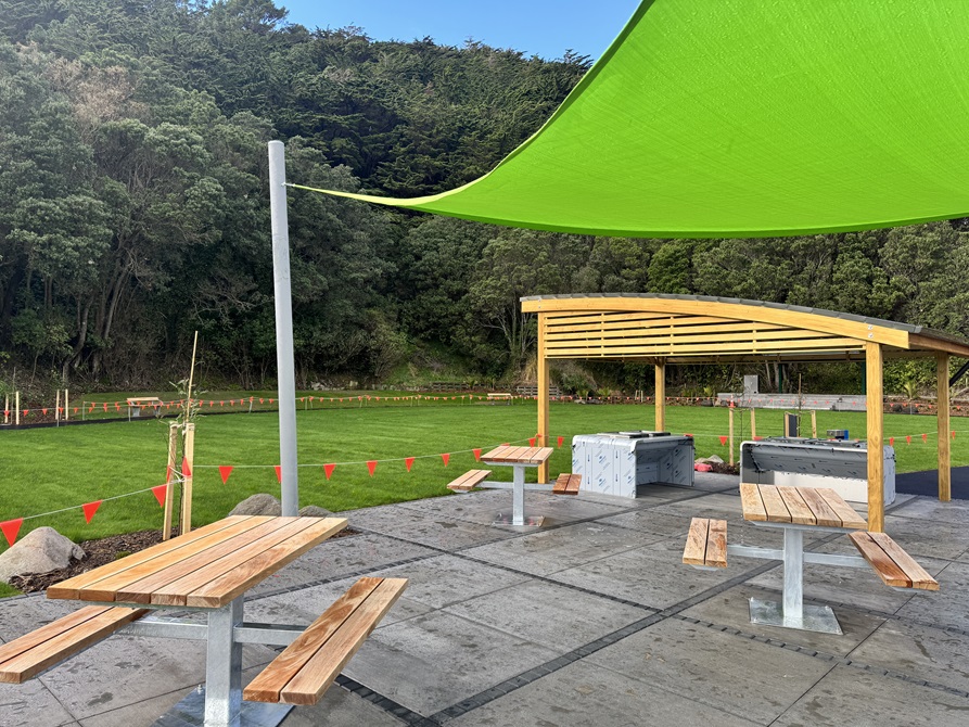 The seating area of the park, with picnic tables and barbeque stations under a decorative wooden shelter.